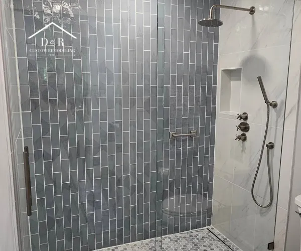 A close-up of a walk-in shower interior showcasing gray vertical subway tiles on the back wall and white marble-style tiles on the side.