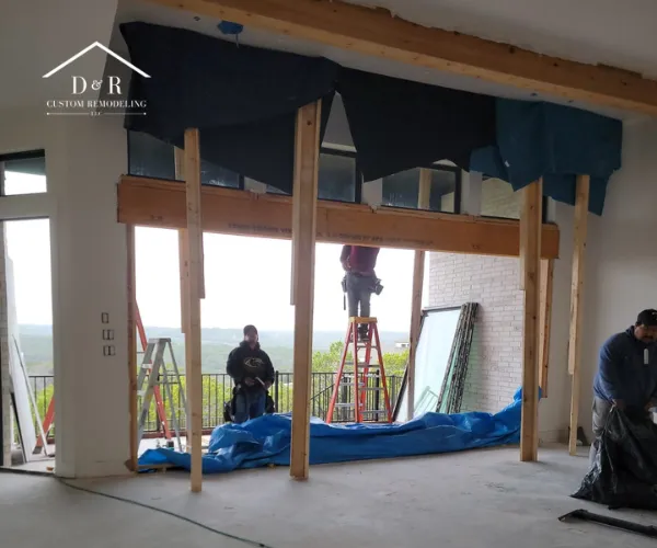 A spacious, open-concept living area with white walls, light wood flooring, and large sliding glass doors leading to a backyard.