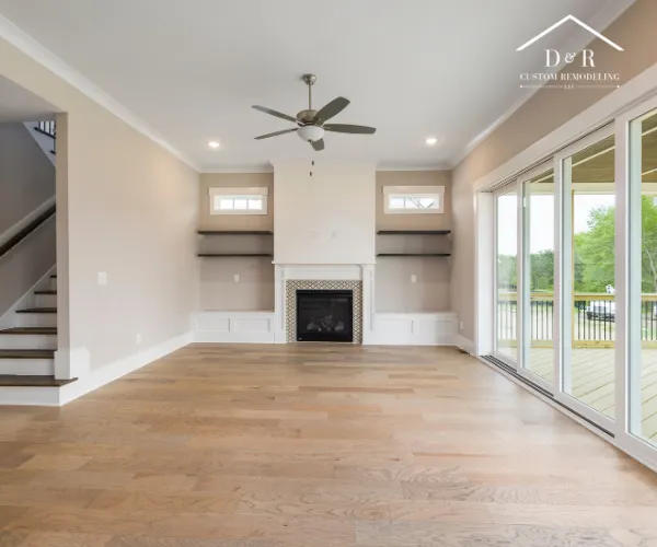 A spacious living room with light hardwood floors, a central fireplace flanked by built-in shelving.