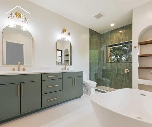 Full view of a remodeled master bathroom featuring a green double vanity, arched mirrors, a glass shower stall, and a white soaking tub.