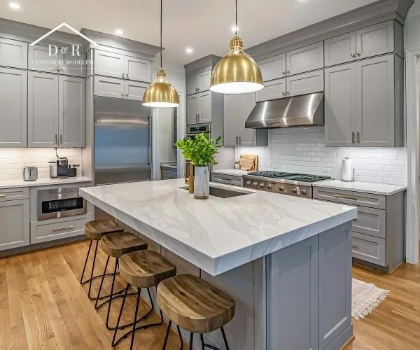 A remodeled kitchen featuring grey cabinetry, a waterfall marble island with wooden barstools, stainless steel appliances, and brass dome pendant lights.